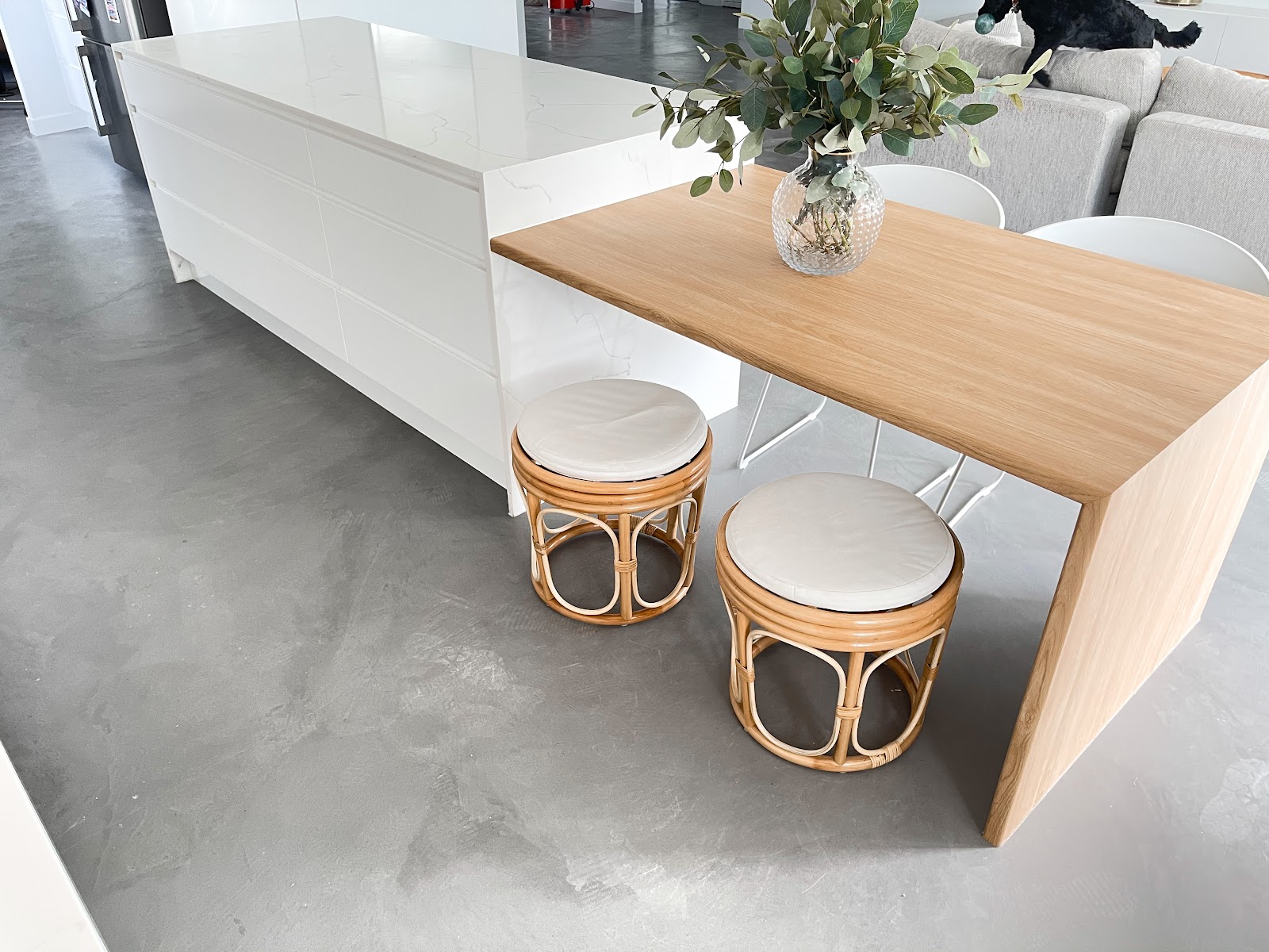Timber waterfall breakfast bench running off a white stone island with rattan stools