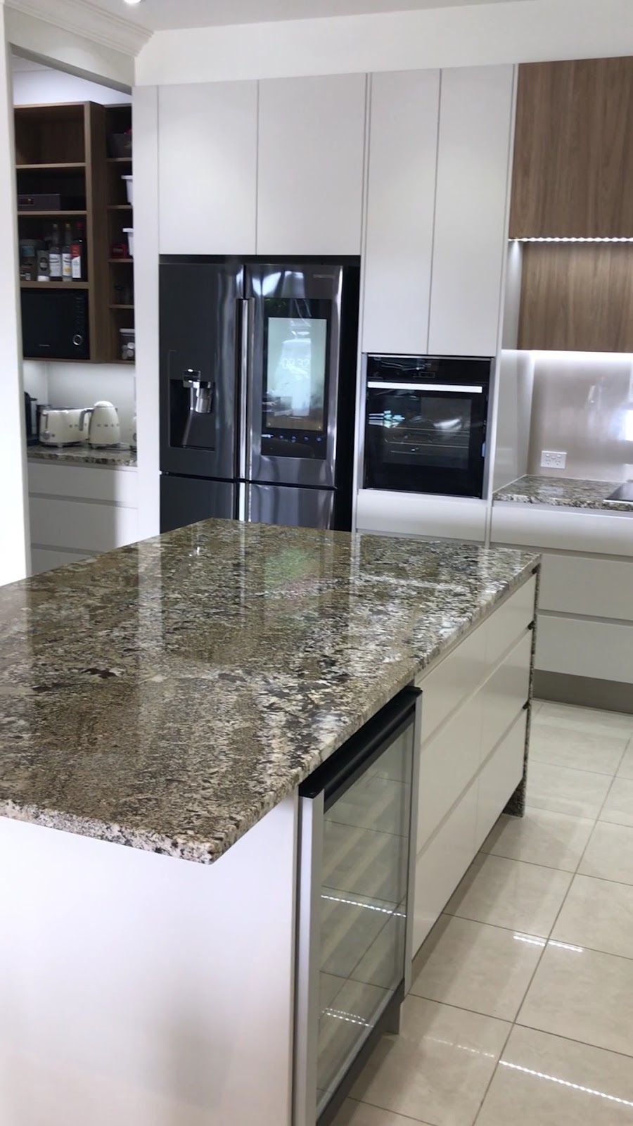 Granite island with a built-in wine fridge beside tall white cabinets