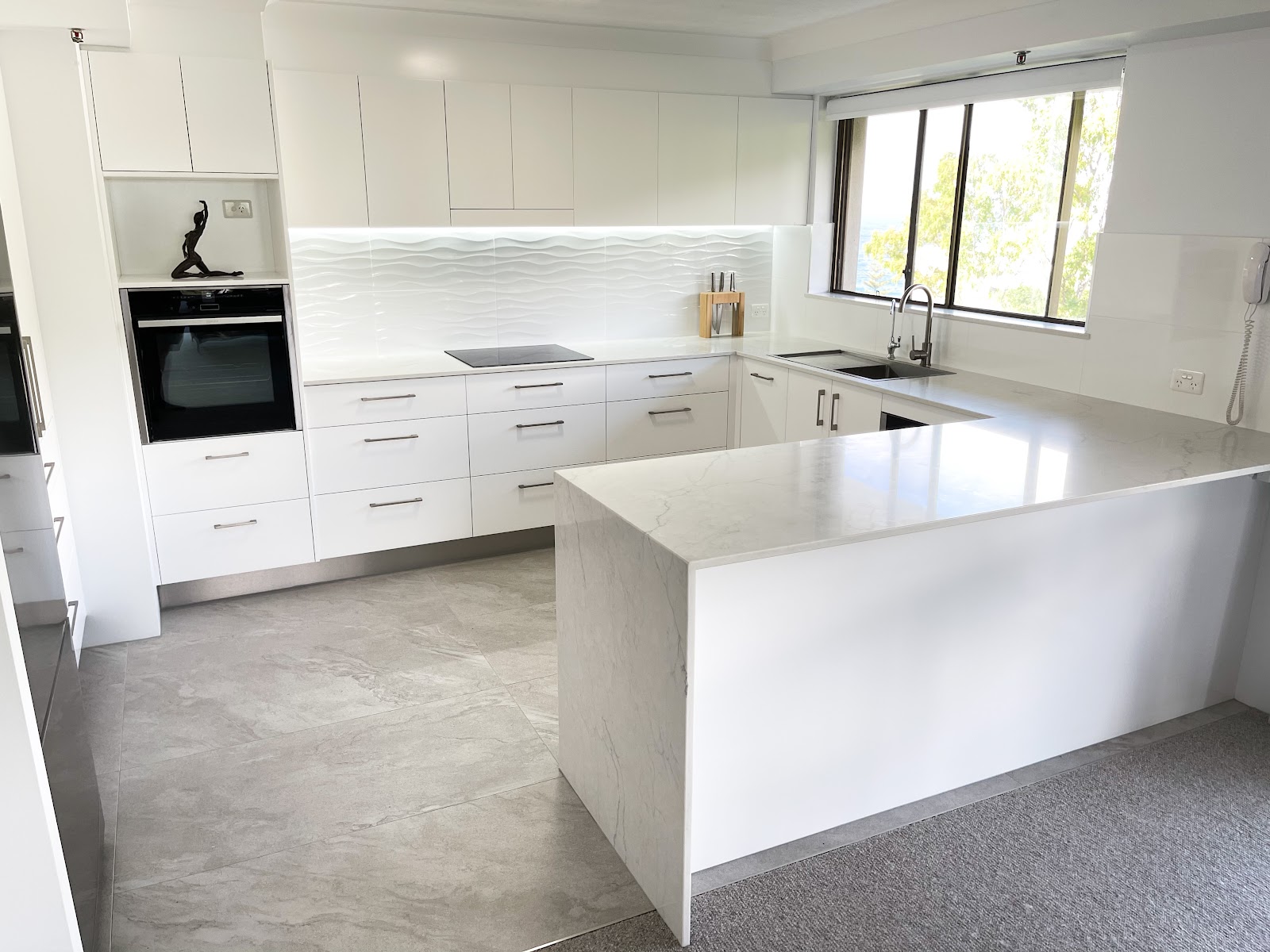 White U-shaped kitchen with a waterfall peninsula and a glimpse of the ocean through the window