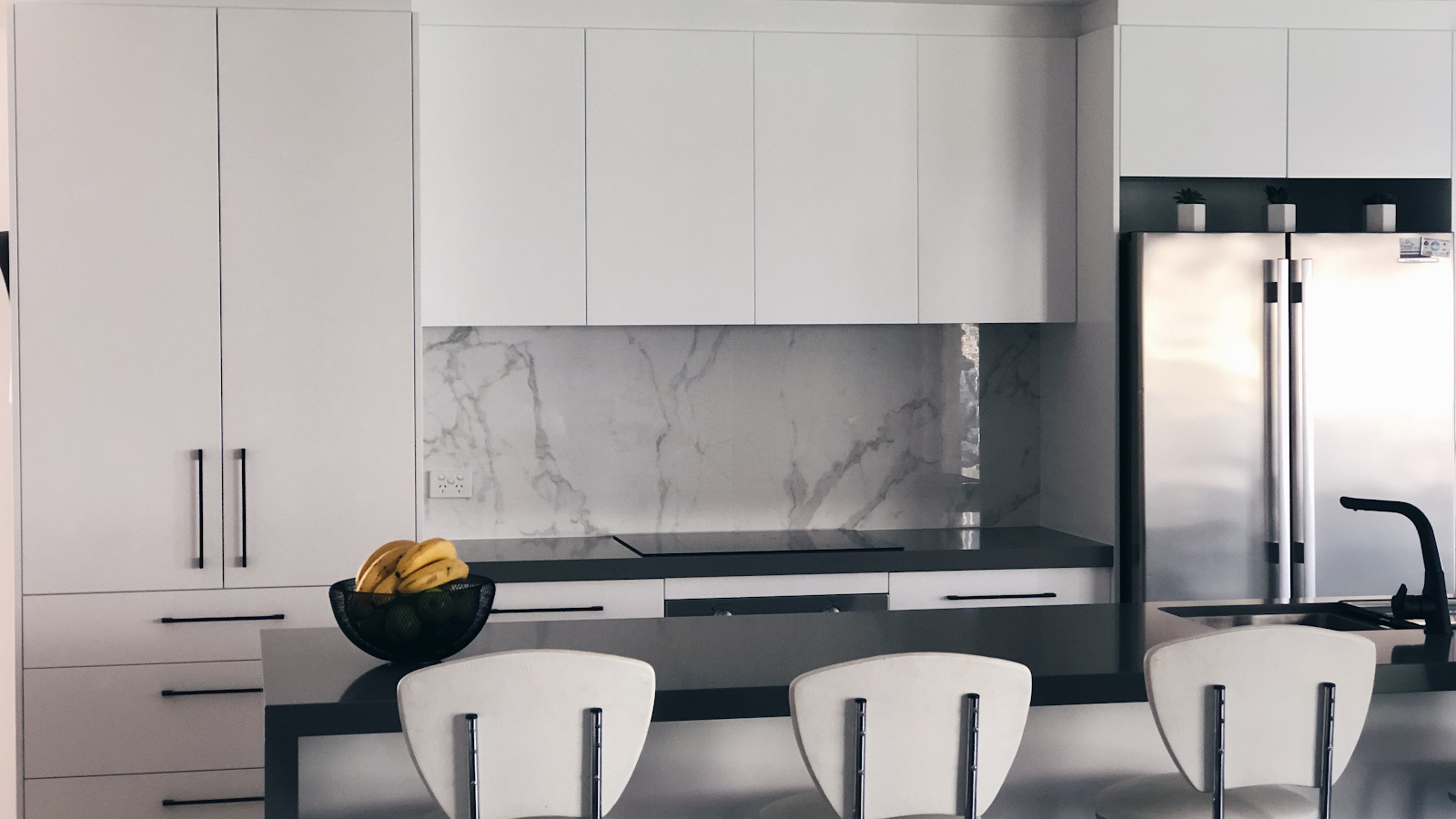 White flat-panel cabinets with a marble slab splashback and a dark island benchtop